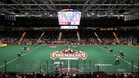 Cancha cubierta de lacrosse con jugadores, árbitros y aficionados.