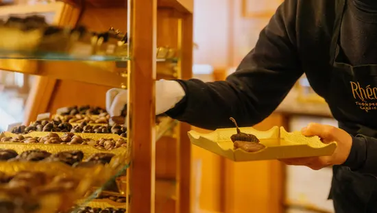 手袋をはめた作業員が陳列ケースからチョコレートを選び、トレイに並べる。