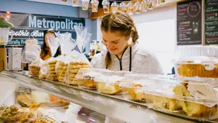 A person wearing a zip up sweater looking at a plethora of pastries and other baked goods at a bakery. 