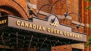 Enseigne portant l’inscription Canadian Opera Company fixée à un édifice en brique, avec supports en métal incurvés et ampoules au-dessus de l’entrée.