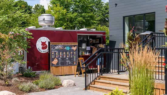 Exterior of the red, Fox in the Hen House food truck surrounded by lush trees.