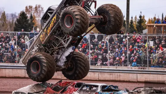 Un camion monstre est suspendu dans les airs au-dessus d'une rangée de voitures écrasées, sous le regard des spectateurs dans les gradins.