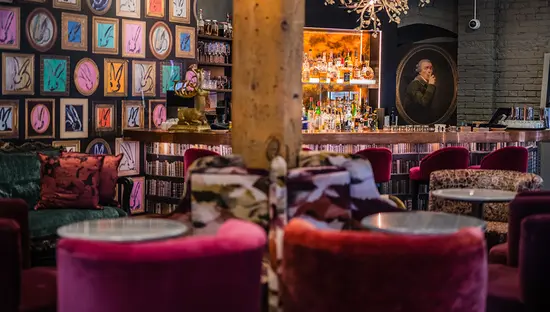 Interior of Secrette, a hidden bar in Toronto, featuring velvet chairs, eclectic art and a cozy, colourful ambiance.
