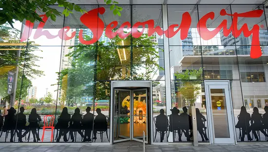L’entrée du cabaret d’humour The Second City à Toronto, en Ontario, où les baies vitrées présentent le nom du cabaret en lettres rouges et des silhouettes de personnes assises en noir.