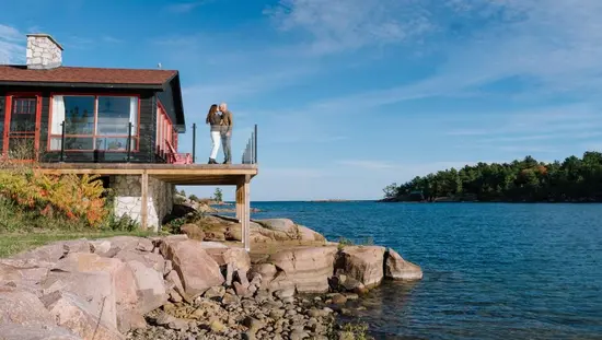 Una pareja se besa en el patio de una acogedora cabaña con vistas a la costa rocosa de la bahía Georgian.