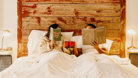 Una pareja lee libros en la cama mientras sostienen tazas.