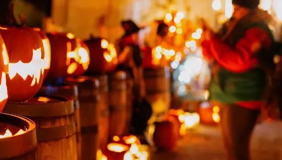 Citrouilles d’Halloween sculptées en lanternes illuminant une rue, avec des gens qui célèbrent en arrière-plan.