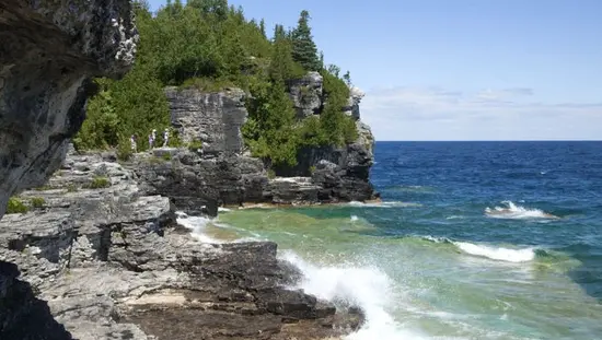 Three people hike along a rocky shoreline overlooking blue water of Georgian Bay.