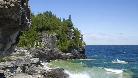 Tres personas caminan a lo largo de una costa rocosa con vistas al agua azul de la Bahía Georgian.