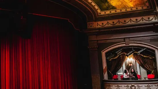 Two women in side balcony seats facing the curtain and stage at the Grand Theatre London.