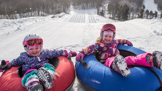 Two children sitting on snow tubes in front of a snowy hill at Horseshoe Resort.