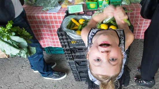 若い女の子がファーマーズマーケットの売り手のテーブルから顔を上げています。