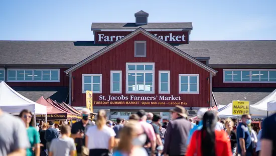 Eine Menschenmenge schlendert bei Tageslicht über den St. Jacobs Farmers' Market.