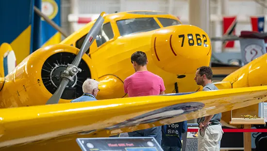 Three people view a vintage aircraft at an aviation museum.