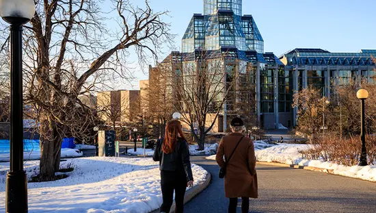 Two women walk towards the National Gallery of Canada in winter.