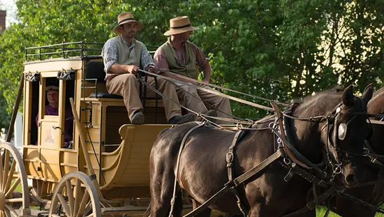 Des employés costumés se promènent à cheval et en calèche dans un village reconstitué du XIXe siècle.