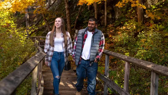 Un couple marche sur une promenade en bois à travers une forêt à l’automne.