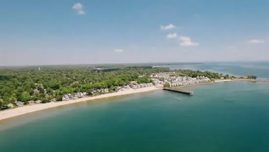 Aerial view of Crystal Beach with soft blue water, sandy shoreline, and rows of charming waterfront homes under a bright sky.