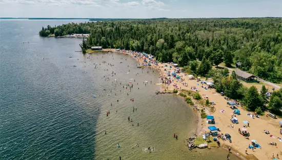 Ein belebter Sommerstrand im Balsam Lake Provincial Park mit Schwimmern und Sonnenschirmen entlang der sandigen Küste.