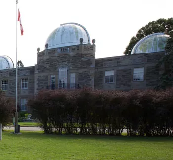 Zwei Gebäude und ein Fahnenmast, Teil des David Dunlap Observatory, sind von einem gepflegten Rasen und Garten umgeben