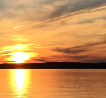 Zwei Angler in einem Boot auf einem großen See unter dramatischem Himmel bei Sonnenuntergang