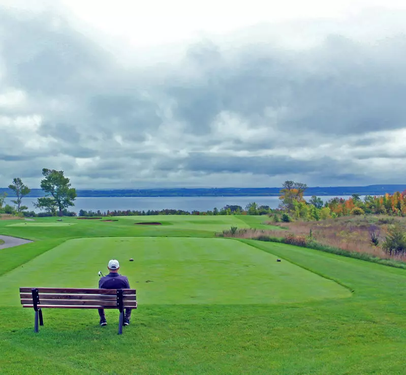 한 남자가 골프장의 그린을 내려다보는 벤치에 앉아 있다.
