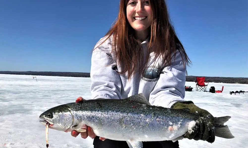 Une femme tient un gros poisson à tête blanche pris sur un lac gelé