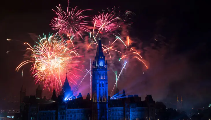 Une femme brandit un drapeau canadien sous un ciel illuminé par des feux d'artifice.