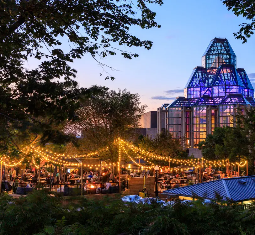 De nombreuses personnes rassemblées en soirée sur une terrasse extérieure, sous des lumières scintillantes, à Ottawa. 