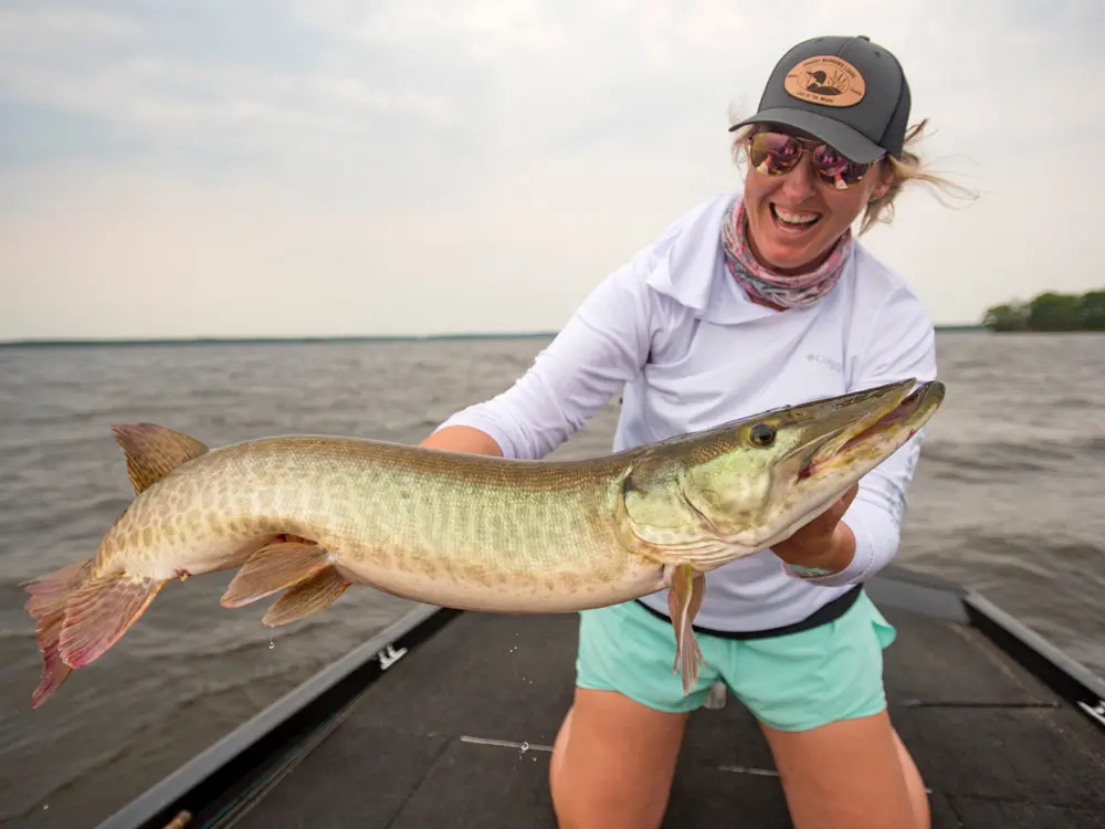 A woman holds up a large muskie on a fishing trip from Grassy Narrows Lodge.