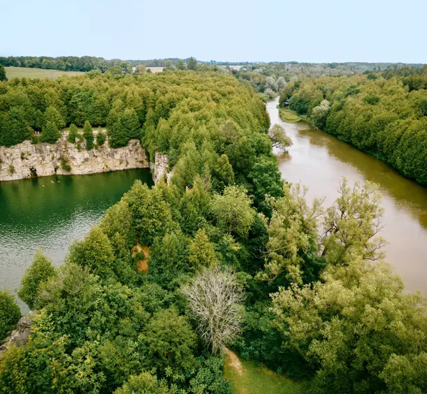 Overhead view of a forested landscape with an emerald quarry lake and curving river.