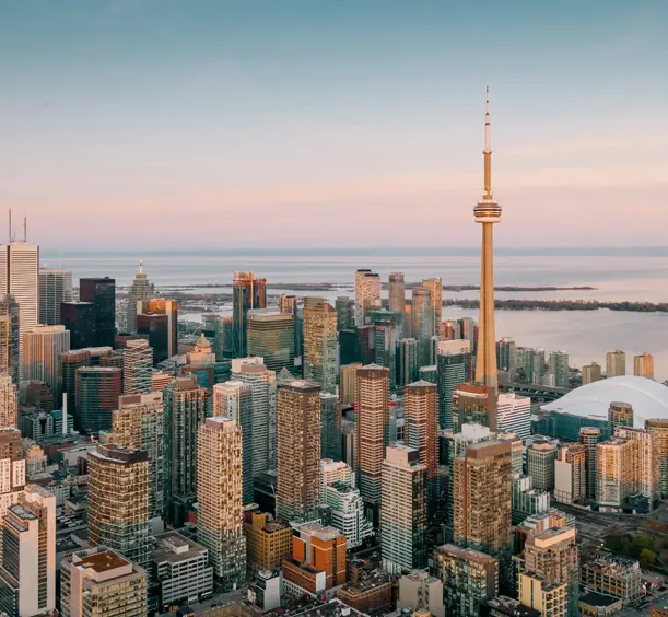 夕焼けの光を浴びた高層ビルや CN タワー、柔らかなパステルカラーの空の下の静かな海を見渡す景色。