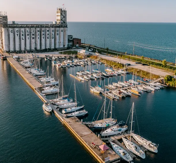 Luftaufnahme der Hafenfront von Collingwood mit den historischen Getreideterminals, in einem Yachthafen ankernden Segelbooten und der Georgian Bay, die sich bis zum Horizont erstreckt.