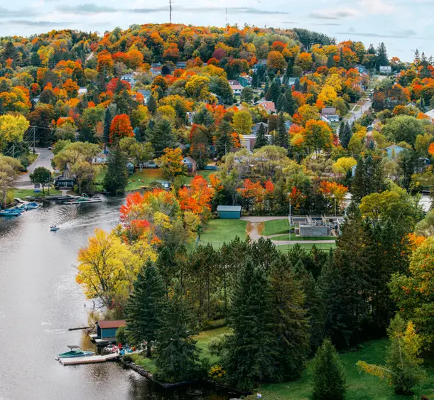 Luftaufnahme von Huntsville, Ontario, mit buntem Herbstlaub rund um den Fluss und der zwischen sanften Hügeln eingebetteten Stadt.