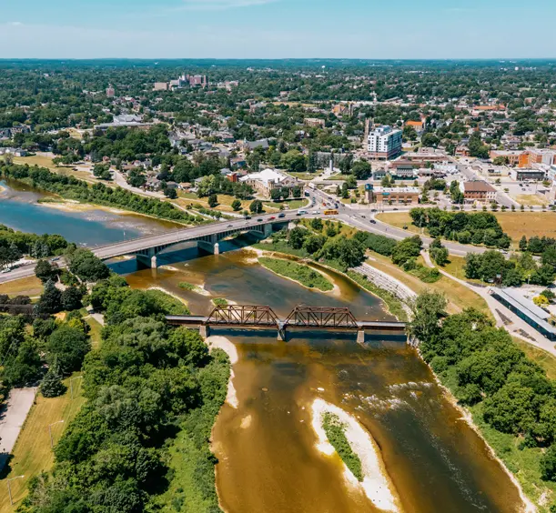 Aerial view of Brantford with Lorne Bridge and rail bridge spanning the Grand River, surrounded by greenery and urban buildings.