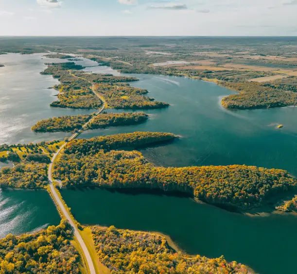 Route sinueuse de Long Sault Parkway traversant des îles boisées sous le soleil, avec les eaux scintillantes du lac s'étendant à perte de vue.