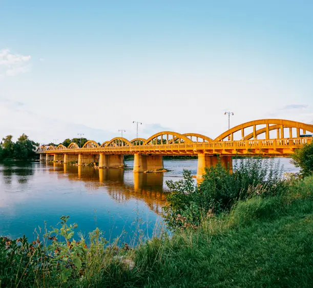 Curved concrete arches of Caledonia’s Argyll Street Bridge glowing at sunset, reflected in the still water with greenery in the foreground.