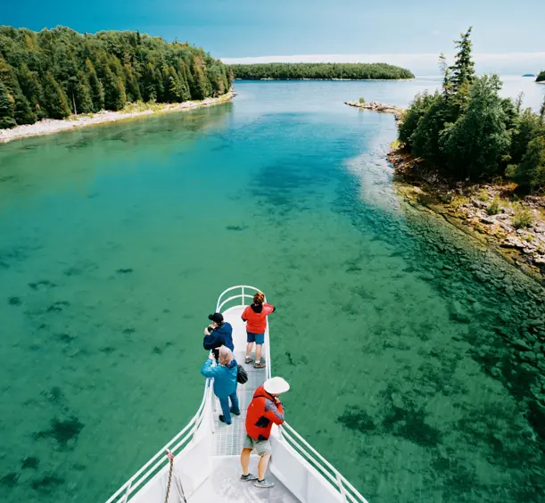 Visitors on a boat cruise through clear turquoise waters near Tobermory on the Bruce Peninsula, surrounded by forested islands.