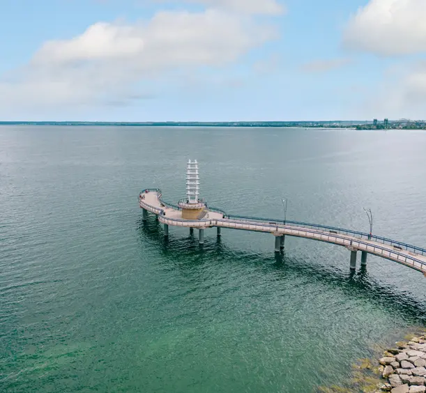 Brant Street Pier curving into the turquoise water of Lake Ontario under a cloudy sky, with visitors walking along the pier.