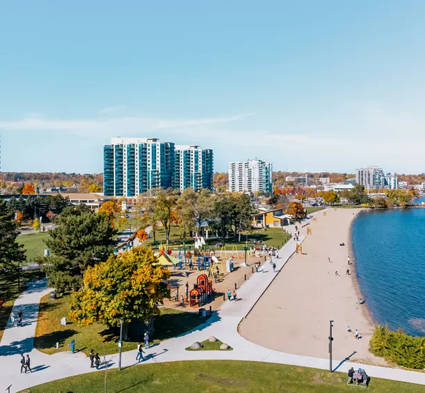 Luftaufnahme des Centennial Park und Strandes in Barrie mit einem Spielplatz, Spazierwegen und einem Sandstrand entlang der Kempenfelt Bay.