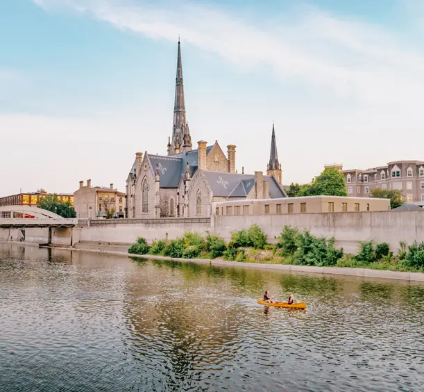 Eine Kanufahrt auf dem Grand River in der Innenstadt von Cambridge, Ontario, vorbei an historischen Gebäuden und Kirchtürmen im Abendlicht.