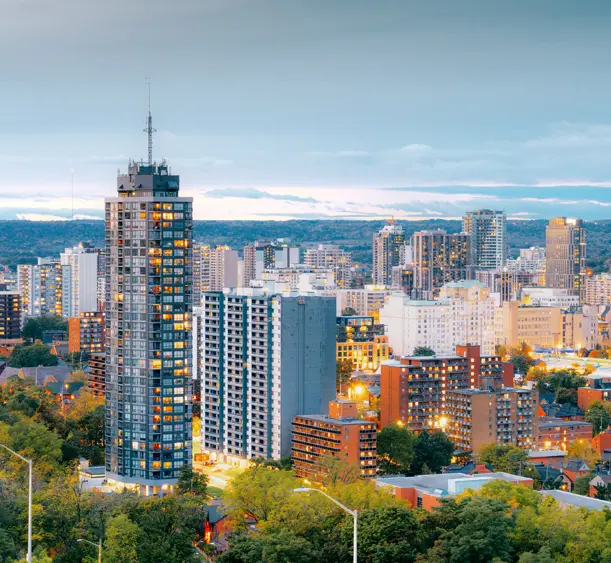 Die Skyline von Hamilton, Ontario, leuchtet zur blauen Stunde, mit Hochhäusern und Bürotürmen, die sich vor einem Abendhimmel abheben.
