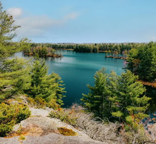 Vue sur le lac entouré d'un relief rocheux et d'une dense forêt de pins au parc provincial Frontenac, par une journée printanière un peu nuageuse.