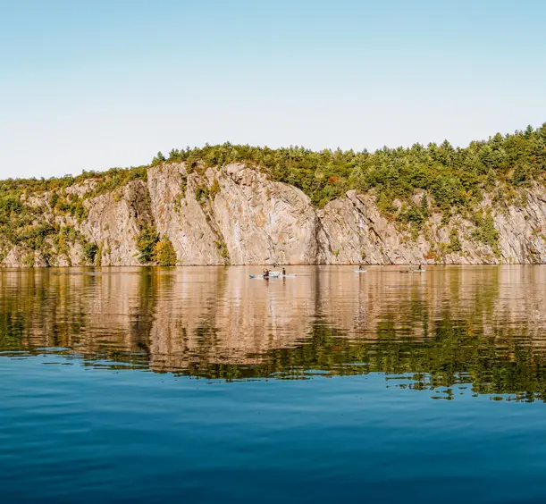 Der hoch aufragende Mazinaw Rock spiegelt sich im Upper Mazinaw Lake, eingerahmt von Wäldern und sandigem Ufer im Bon Echo Provincial Park.