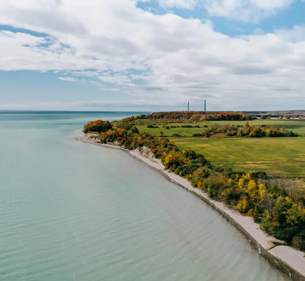 Turquoise water along the Port Hope shoreline in Northumberland, with lush greenery and a cloudy blue sky overhead.