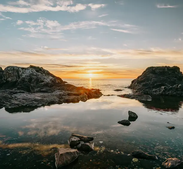 Sunset over Lake Superior near Sawpit Bay in Batchawana Bay, Ontario, with dark rocky outcrops reflected in the calm water.
