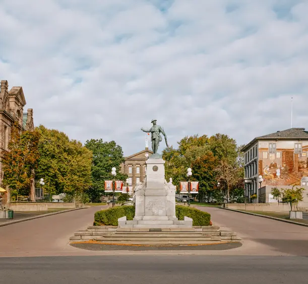 Centre-ville historique de Brockville avec un monument commémoratif central, des bâtiments patrimoniaux et des rues bordées d'arbres sous les nuages.