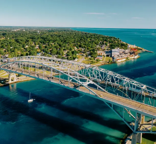Aerial view of Blue Water Bridge spanning the bright blue St. Clair River, connecting Sarnia and Port Huron, with a lush green shoreline.