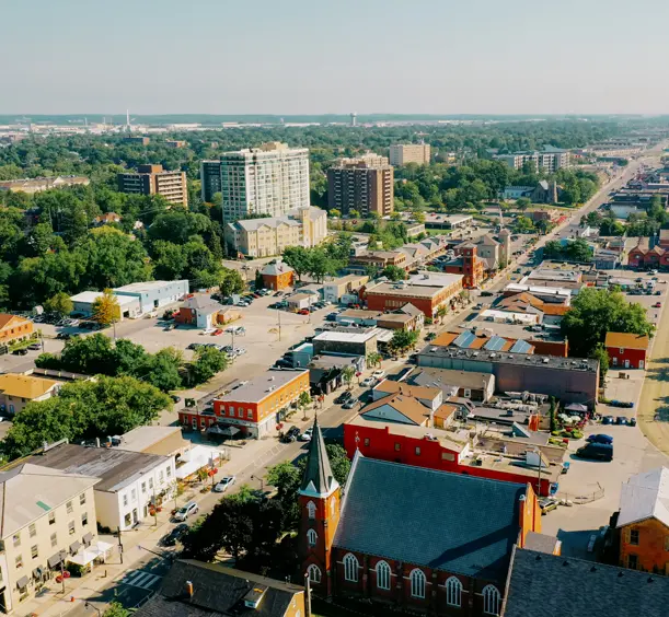 Aerial view of downtown Milton, with historic buildings, tree-lined streets and mid-rise residential properties on a sunny day.