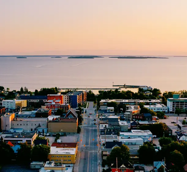 Aerial view of downtown North Bay at dusk, with the glowing waterfront and Manitou Islands visible in the distance.